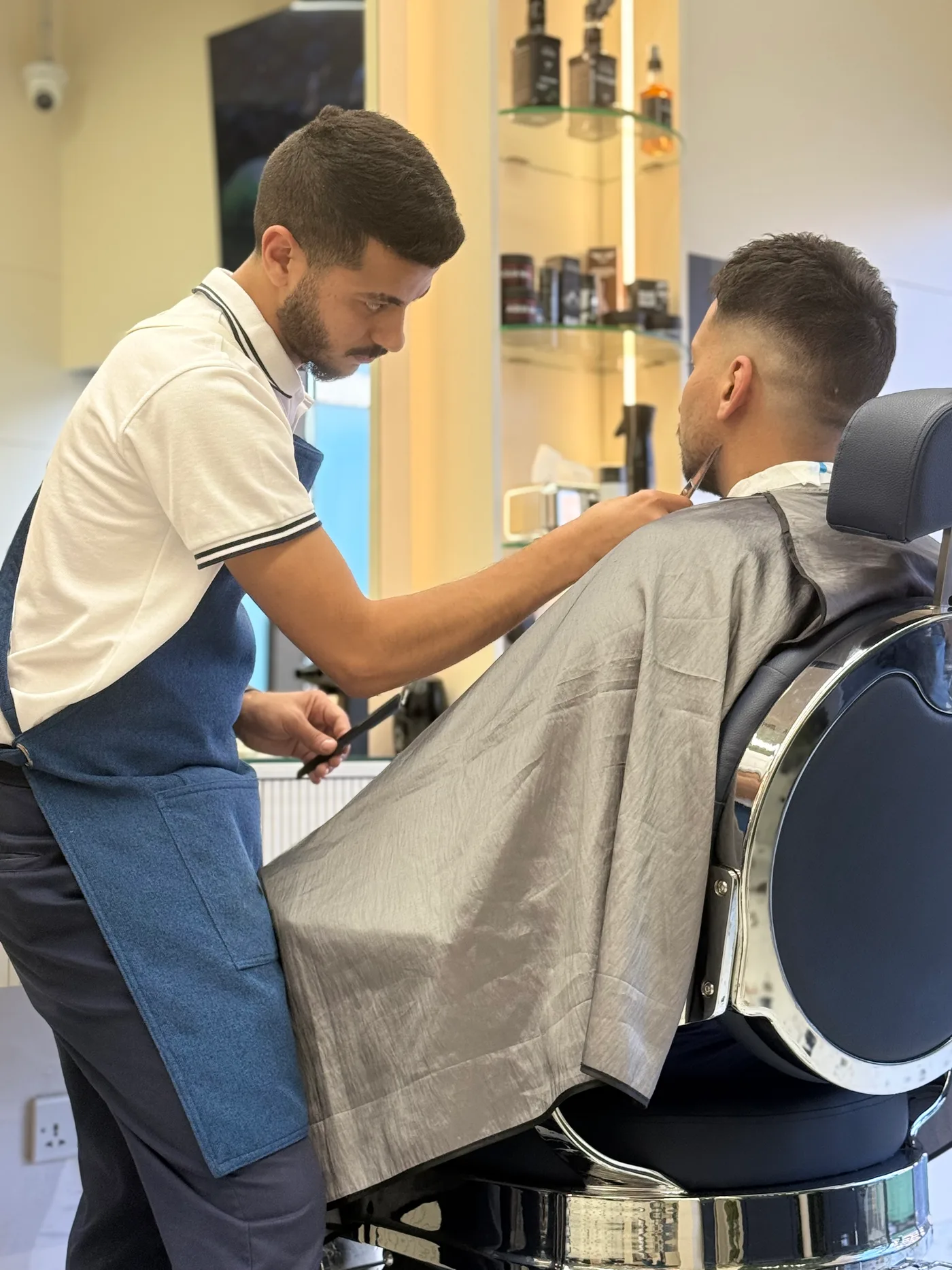 Barber cutting hair at a chrome barber chair inside Spazio Gents Salon, JVC