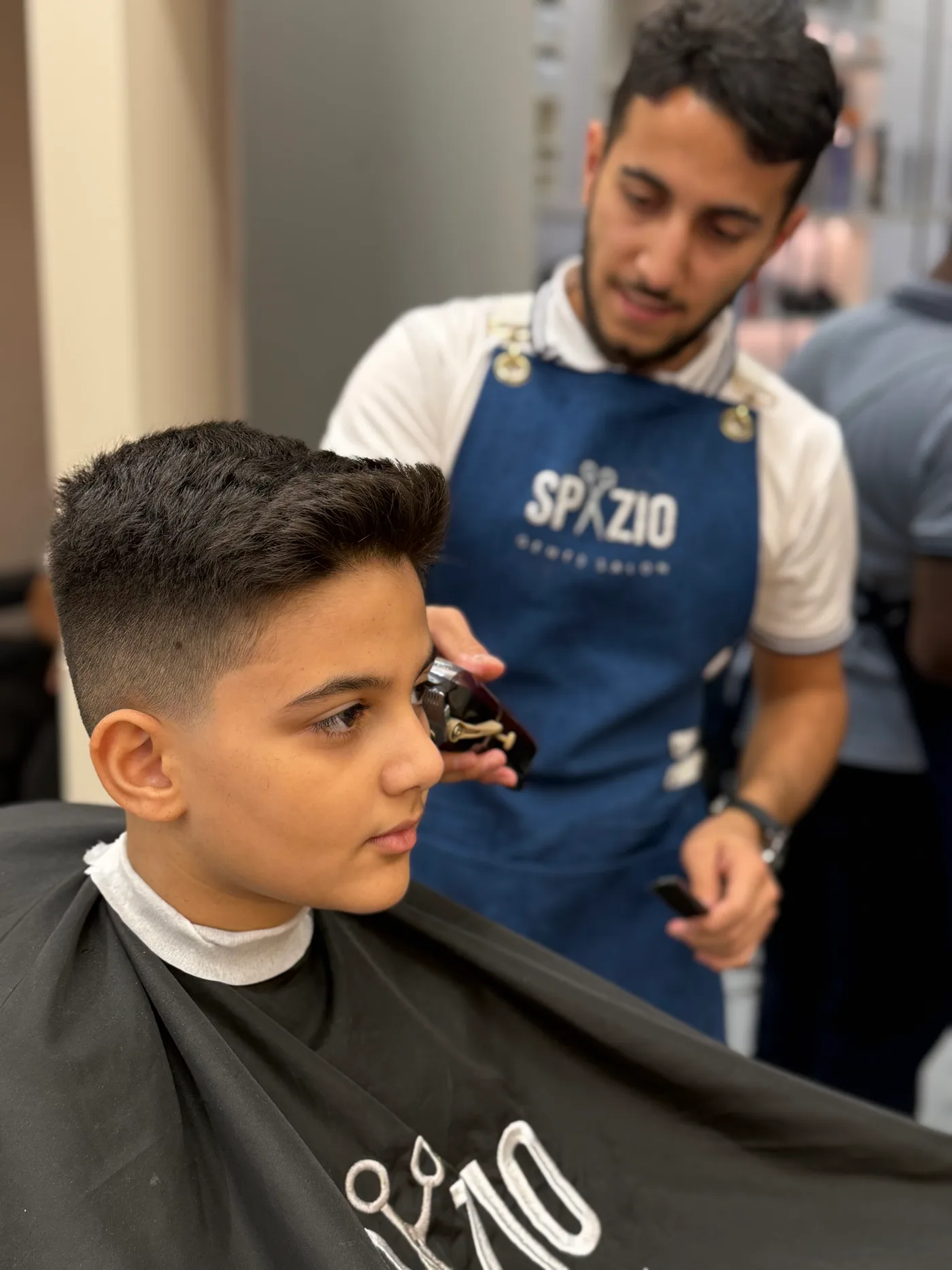 Barber in a Spazio apron trimming a boy's haircut at Spazio Gents Salon in JVC, Dubai