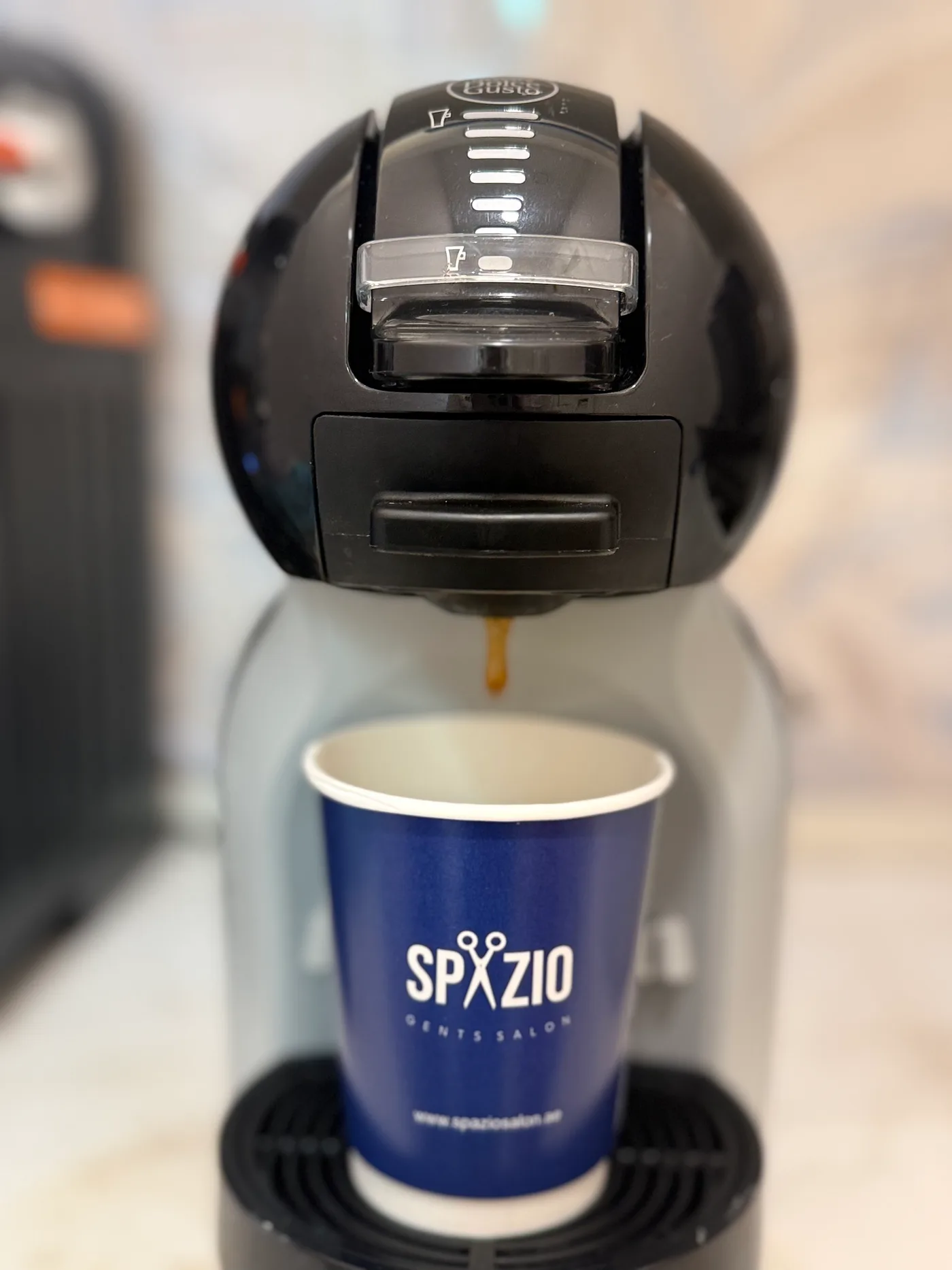 Coffee machine pouring an espresso into a Spazio Gents Salon branded cup in JVC, Dubai