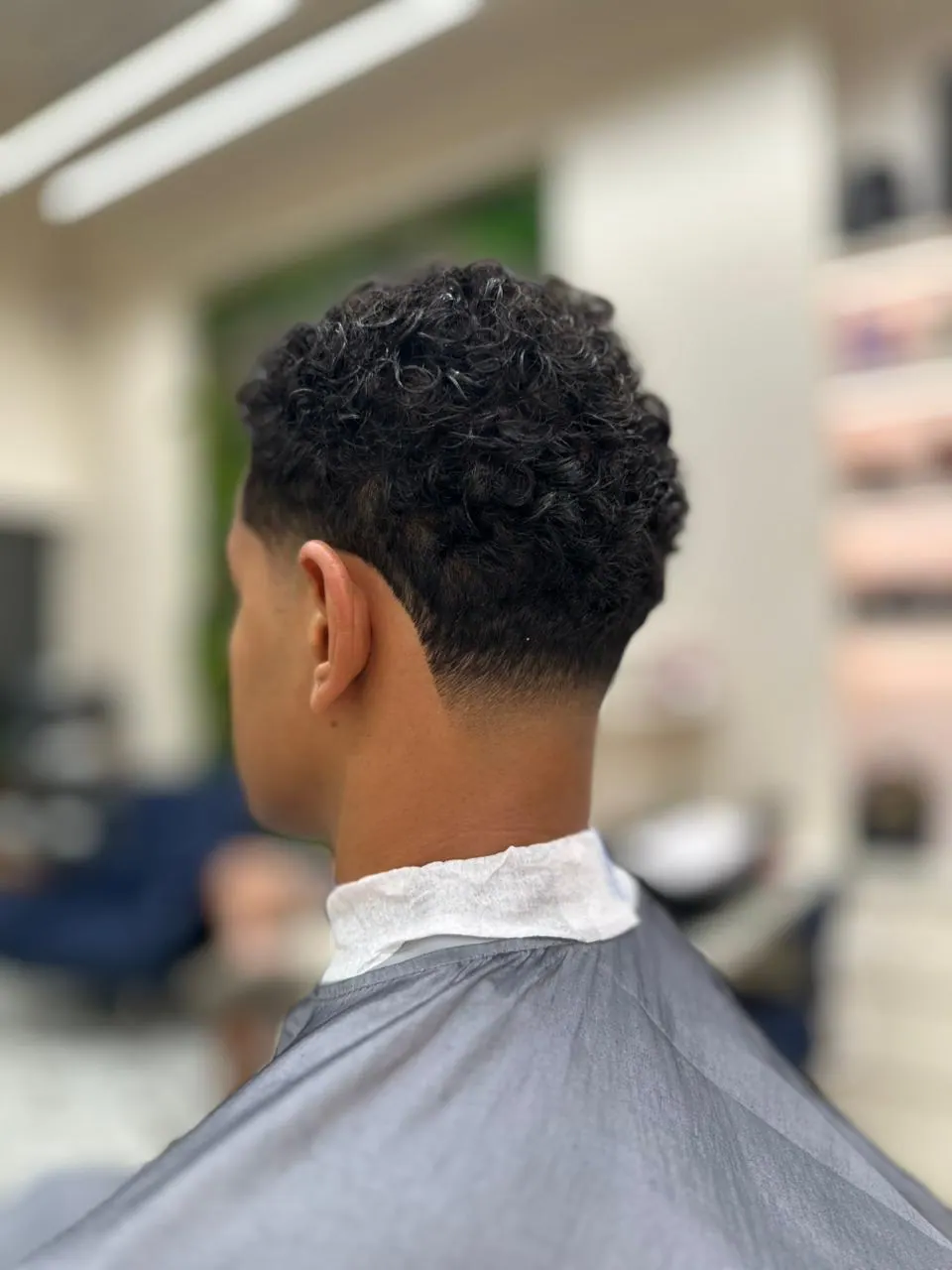 Back view of a curly hair cut, tapered at the neck, at Spazio Gents Salon in JVC