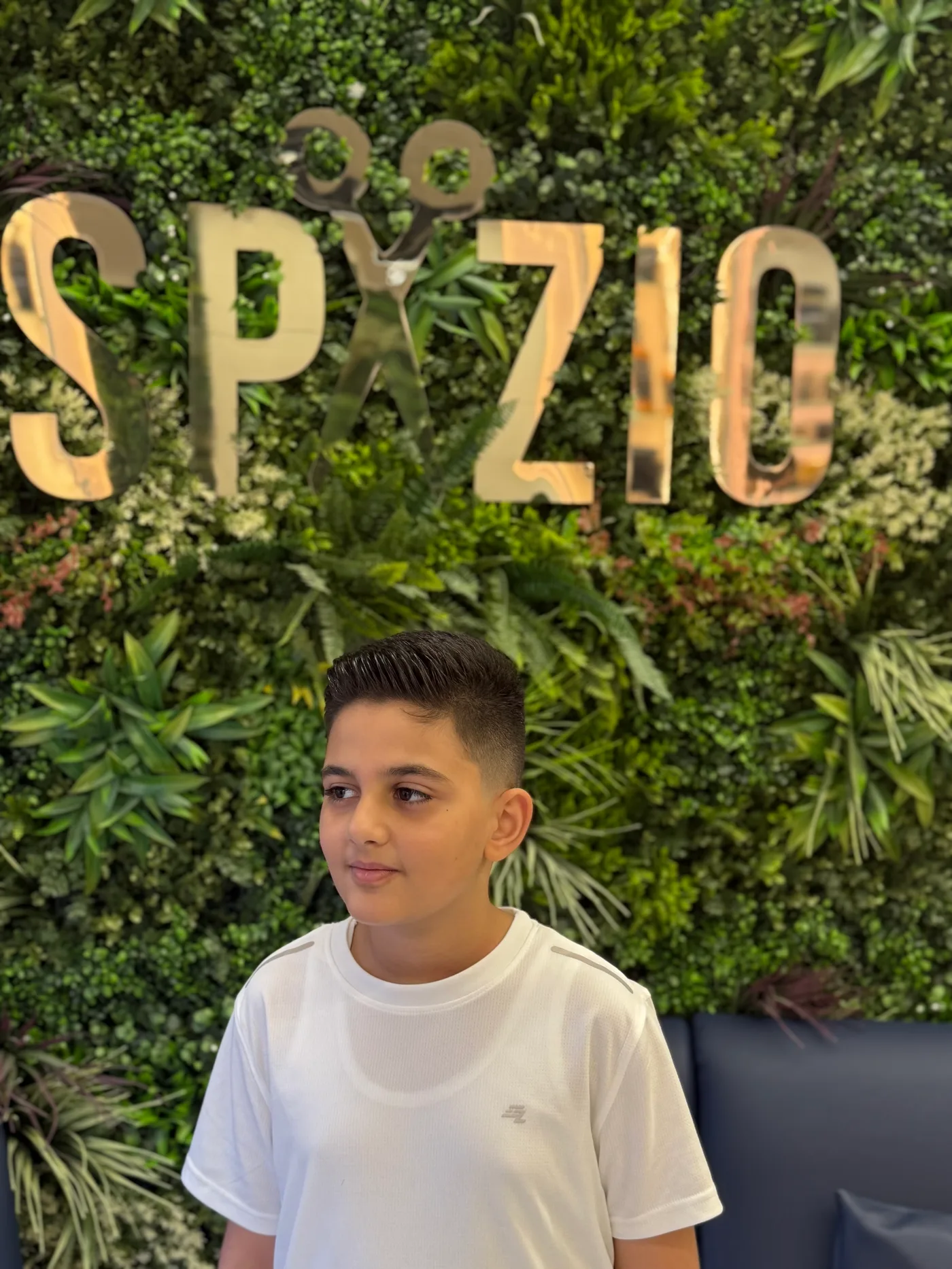 Boy with a finished kids haircut in front of the Spazio green wall in Jumeirah Village Circle